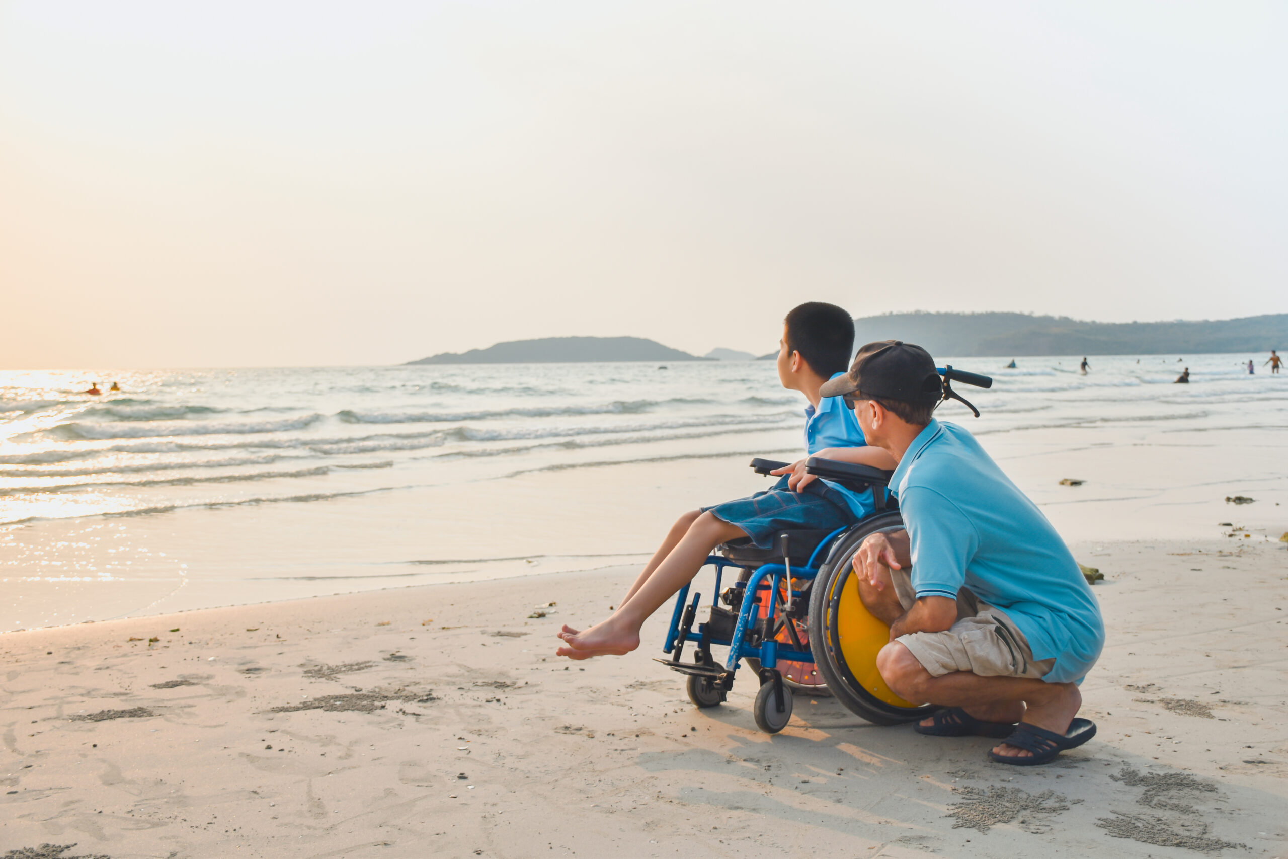 Asian special child on wheelchair and his dad on the beach at sunset, Father helped him to get closer to nature, Life in the education age of disabled children, Happy disabled kid concept.